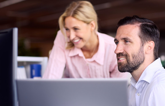 Kaksi henkilöä toimistolla tietokoneen ääressä.